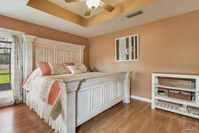 bedroom with light hardwood / wood-style floors, ceiling fan, and a tray ceiling