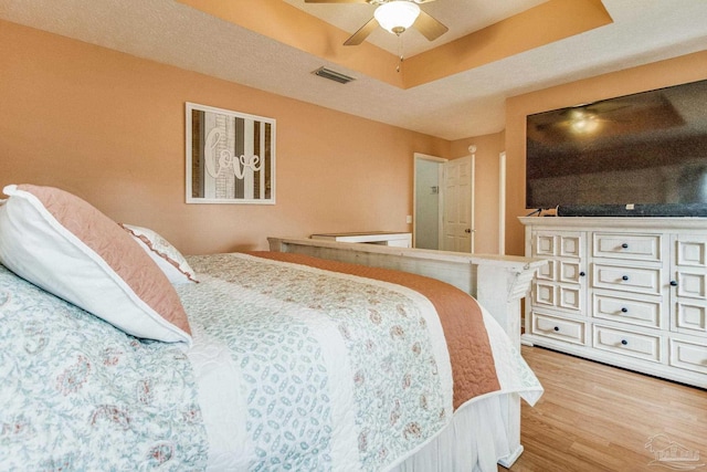 bedroom with a raised ceiling, ceiling fan, and light wood-type flooring