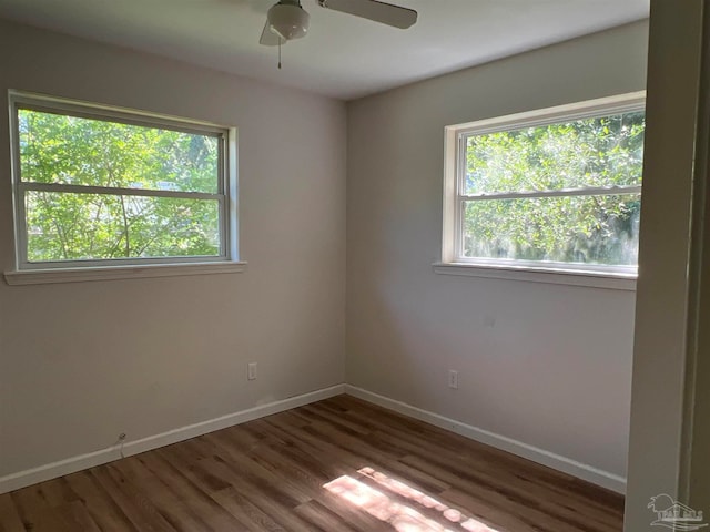 empty room with ceiling fan, plenty of natural light, dark hardwood / wood-style floors, and a water view