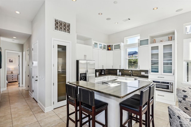 kitchen featuring a kitchen bar, appliances with stainless steel finishes, light tile patterned floors, white cabinets, and a center island