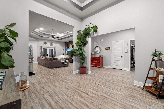 living room featuring french doors, ornamental molding, a raised ceiling, ceiling fan, and light hardwood / wood-style flooring