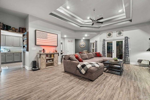 living room with french doors, a raised ceiling, ceiling fan, crown molding, and light hardwood / wood-style flooring