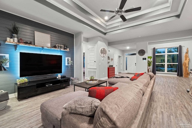 living room featuring a tray ceiling, crown molding, wooden walls, and light wood-type flooring