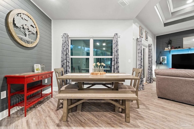 dining room featuring vaulted ceiling, wood walls, and light wood-type flooring