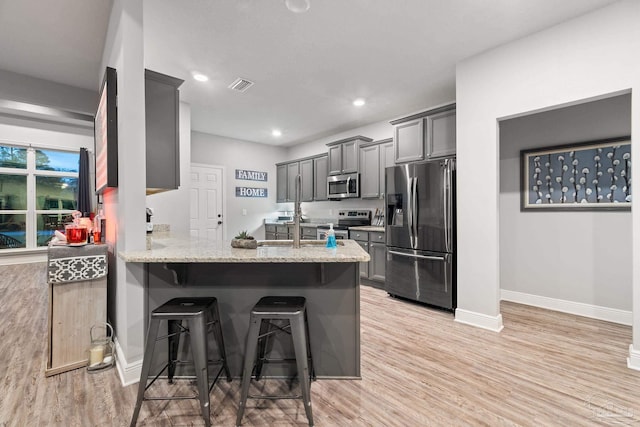 kitchen with kitchen peninsula, light wood-type flooring, a breakfast bar, stainless steel appliances, and gray cabinets