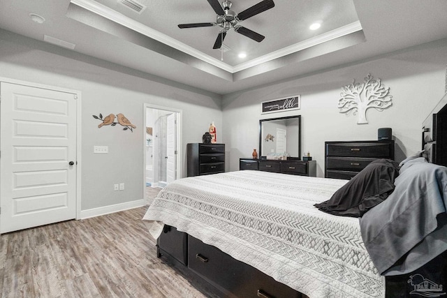 bedroom with ensuite bathroom, crown molding, light hardwood / wood-style floors, ceiling fan, and a raised ceiling