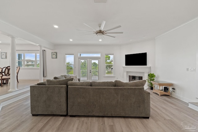 living room featuring ceiling fan, crown molding, light hardwood / wood-style floors, ornate columns, and a tiled fireplace