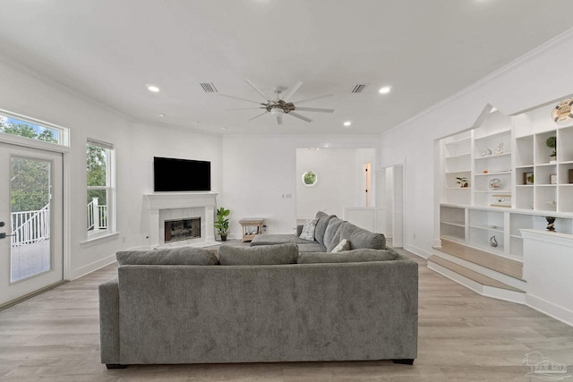 living room featuring crown molding, a tiled fireplace, light hardwood / wood-style flooring, and ceiling fan