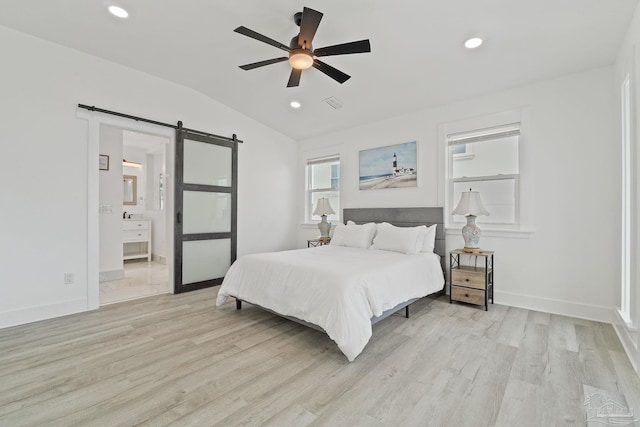 bedroom featuring lofted ceiling, a barn door, ceiling fan, light hardwood / wood-style floors, and ensuite bathroom