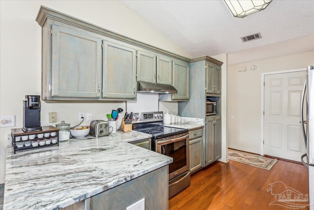 kitchen with appliances with stainless steel finishes, lofted ceiling, light stone countertops, dark wood-type flooring, and a textured ceiling