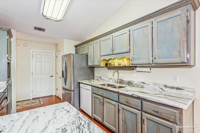 kitchen featuring sink, vaulted ceiling, dishwasher, hardwood / wood-style flooring, and light stone countertops