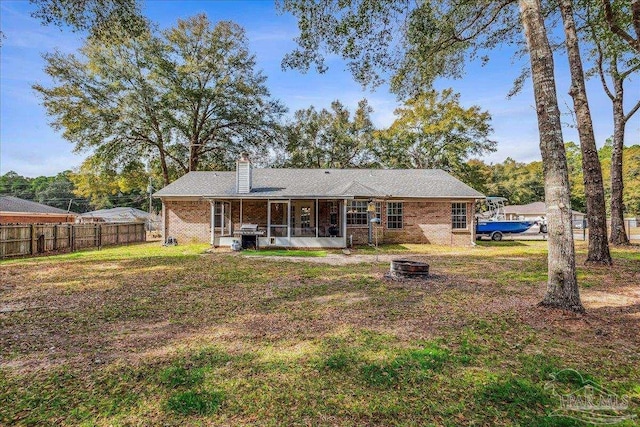 back of property with an outdoor fire pit, a yard, and a sunroom