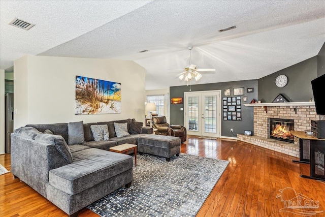 living room featuring lofted ceiling, a brick fireplace, wood-type flooring, and french doors