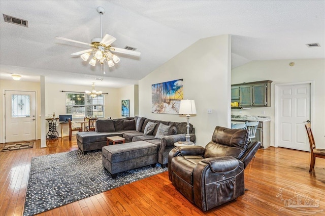 living room with lofted ceiling, hardwood / wood-style flooring, ceiling fan with notable chandelier, and a textured ceiling