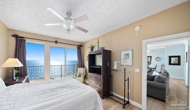 bedroom featuring ceiling fan, a water view, light wood-style flooring, and baseboards