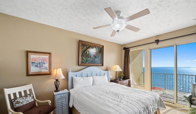 bedroom featuring access to exterior, a water view, a textured ceiling, and a ceiling fan