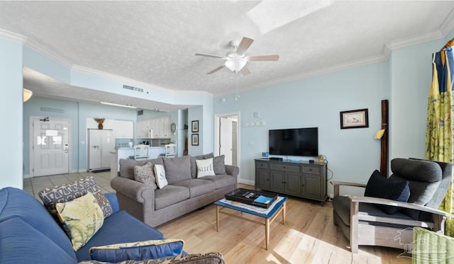 living room featuring light wood-style floors, a textured ceiling, visible vents, and crown molding