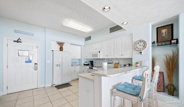 kitchen with light tile patterned floors, a peninsula, white appliances, white cabinetry, and light countertops