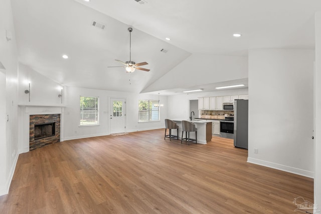 5473 Tucker Cir, Pace, FL 32571 - unfurnished living room featuring high vaulted ceiling, a ceiling fan, a stone fireplace, light wood-type flooring, and baseboards