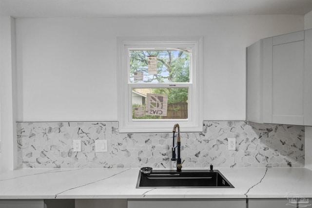 kitchen with white cabinets, decorative backsplash, light stone counters, and sink