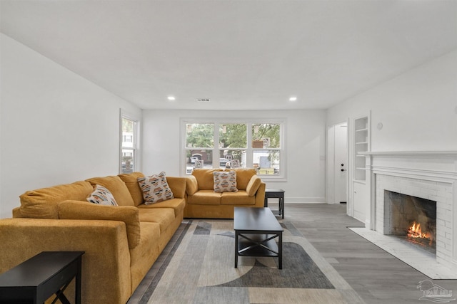 living room featuring a brick fireplace, built in shelves, and hardwood / wood-style flooring