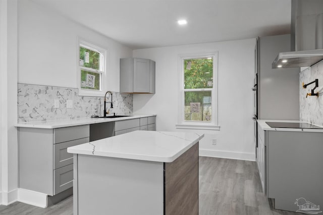 kitchen featuring backsplash, wall chimney exhaust hood, sink, gray cabinets, and a kitchen island