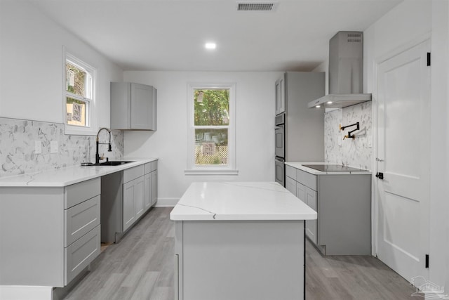 kitchen featuring gray cabinetry, black electric stovetop, wall chimney range hood, sink, and light hardwood / wood-style flooring