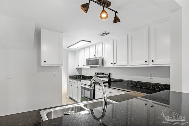 kitchen with white cabinets, stainless steel appliances, and dark stone counters