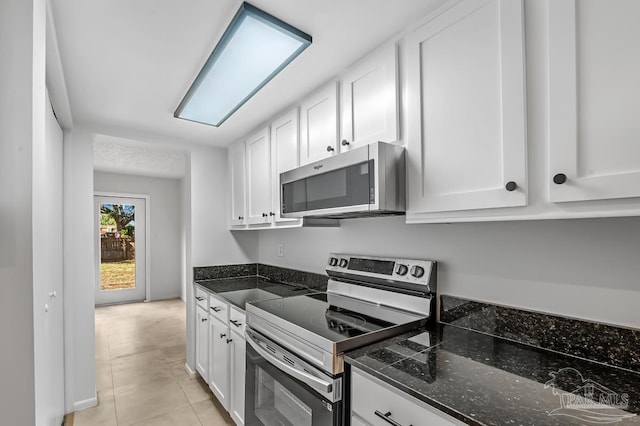 kitchen with white cabinetry, appliances with stainless steel finishes, dark stone counters, and light tile patterned flooring