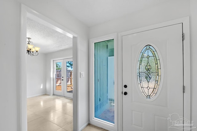 tiled foyer entrance featuring a notable chandelier, french doors, plenty of natural light, and a textured ceiling