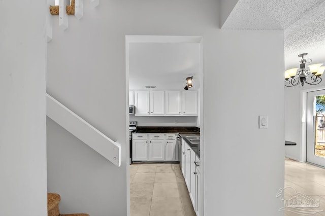 kitchen with a textured ceiling, appliances with stainless steel finishes, white cabinetry, an inviting chandelier, and light tile patterned floors