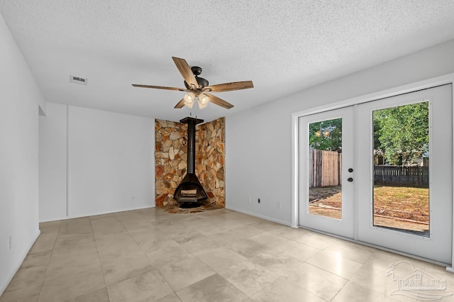 unfurnished living room featuring ceiling fan, a textured ceiling, a wood stove, and french doors