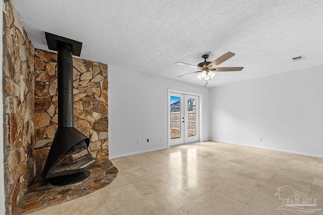 unfurnished living room with ceiling fan, a wood stove, a textured ceiling, and french doors