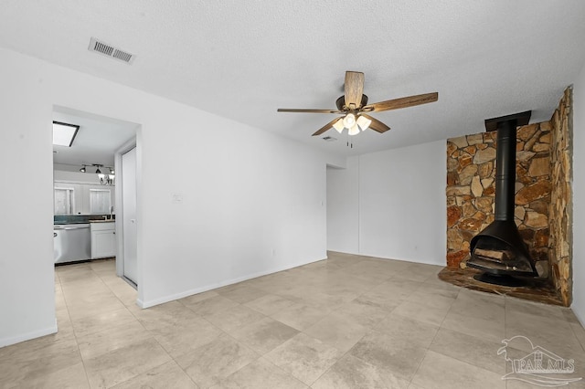 unfurnished living room featuring a wood stove, ceiling fan, and a textured ceiling