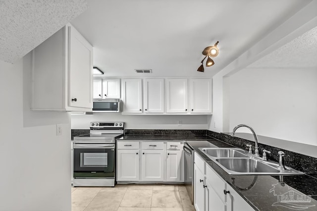 kitchen featuring white cabinetry, stainless steel appliances, dark stone countertops, sink, and light tile patterned flooring