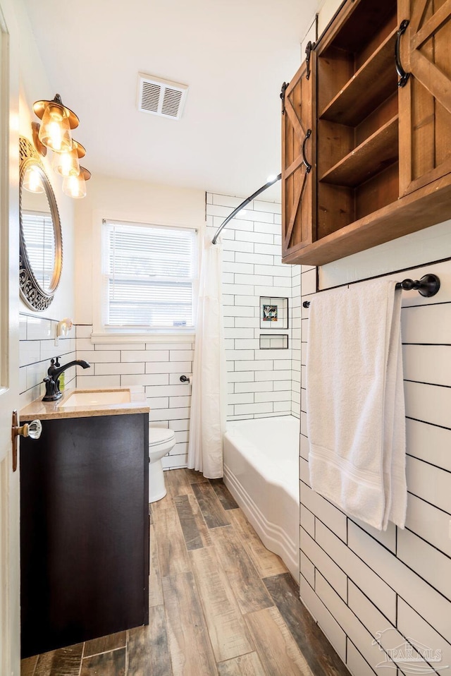 full bathroom featuring vanity, shower / bath combo with shower curtain, wood-type flooring, tile walls, and toilet