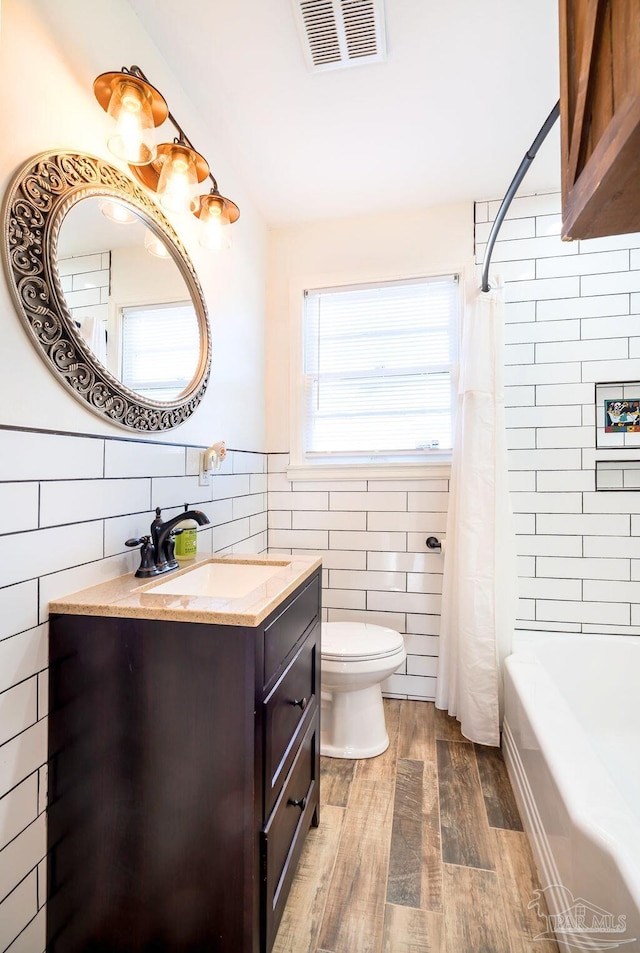 full bathroom with tile walls, wood-type flooring, toilet, vanity, and shower / tub combo