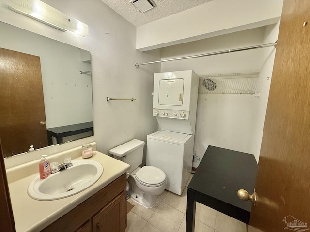 bathroom with stacked washer / dryer, vanity, toilet, tile patterned floors, and a textured ceiling