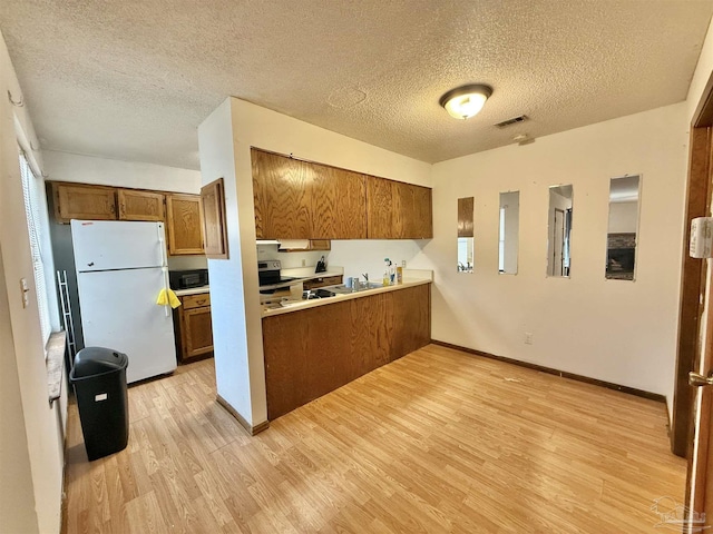 kitchen featuring white fridge, a textured ceiling, light hardwood / wood-style floors, and kitchen peninsula