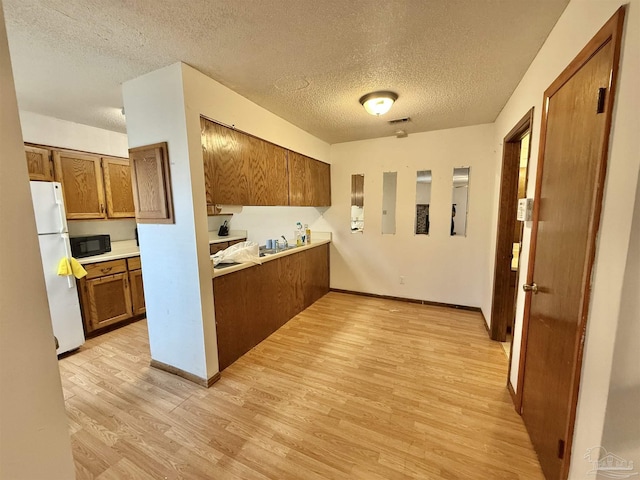 kitchen featuring light hardwood / wood-style floors, a textured ceiling, and white fridge