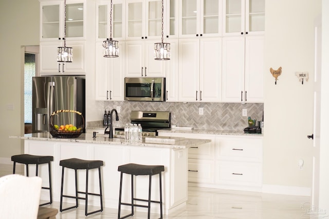 kitchen featuring pendant lighting, white cabinets, decorative backsplash, light stone counters, and stainless steel appliances