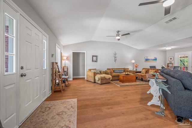 living area with visible vents, baseboards, ceiling fan, light wood-style floors, and lofted ceiling