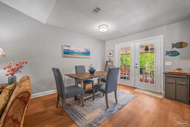 dining room featuring visible vents, baseboards, light wood-type flooring, a textured ceiling, and french doors