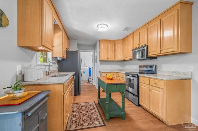 kitchen featuring light wood-type flooring, visible vents, appliances with stainless steel finishes, light stone counters, and a sink
