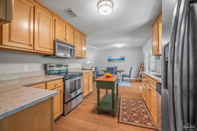 kitchen featuring visible vents, light countertops, light wood-style floors, a textured ceiling, and stainless steel appliances