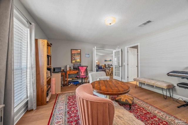 living room featuring french doors, visible vents, light wood-style flooring, and a textured ceiling