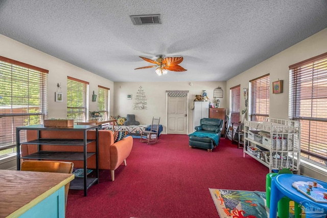 carpeted living room featuring a wealth of natural light, visible vents, a textured ceiling, and ceiling fan