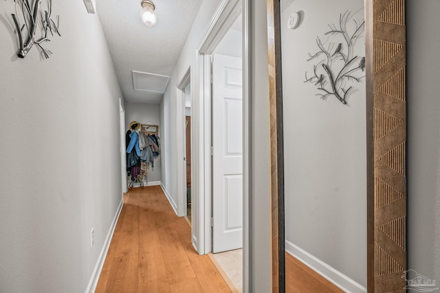 hallway featuring light wood-type flooring, attic access, baseboards, and a textured ceiling