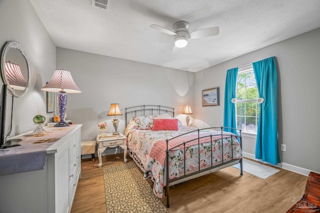 bedroom with baseboards, light wood-type flooring, a textured ceiling, visible vents, and ceiling fan