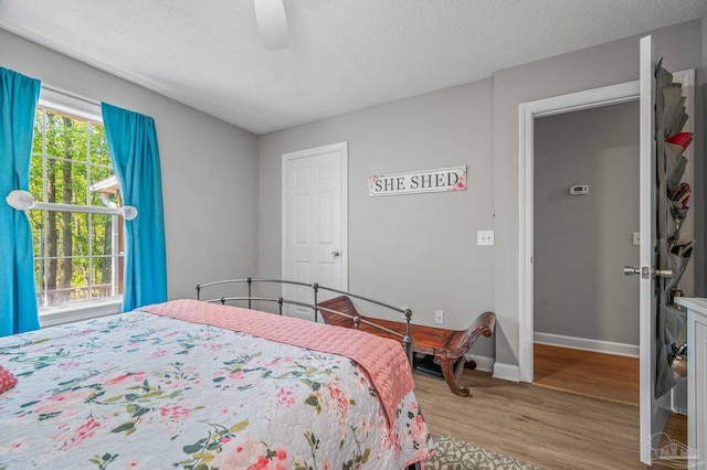 bedroom featuring light wood-style flooring, ceiling fan, baseboards, and a textured ceiling